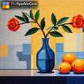A needlepoint canvas design featuring a blue vase with green leaves and two red roses, alongside three oranges, set against a yellow and blue geometric background. The brand logo 'TheSparkleGrid' is visible in the top left corner.
